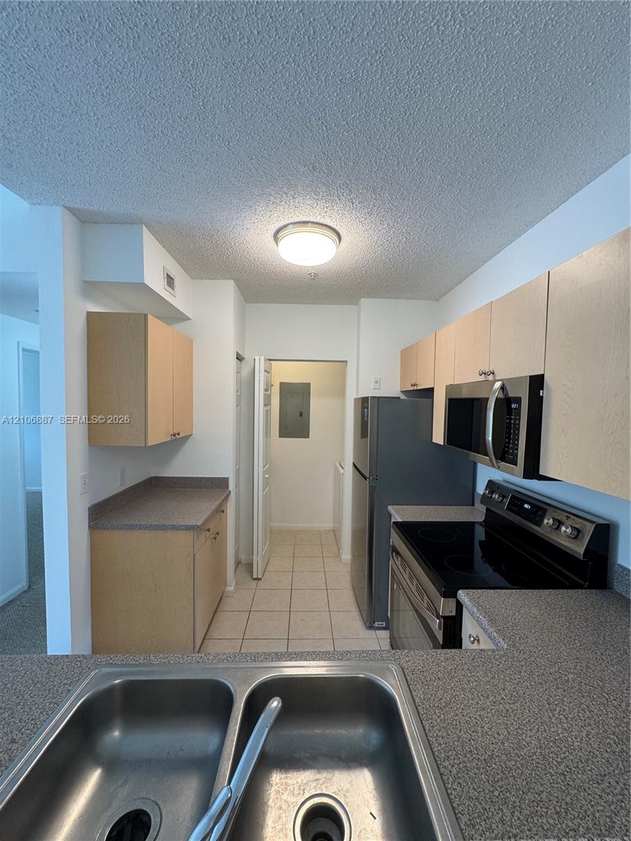 Kitchen featuring light-finish cabinetry, neutral solid-surface countertops, dual-basin stainless steel sink, and integrated microwave