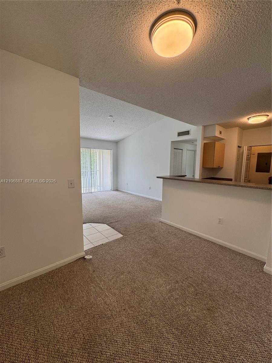 Interior space featuring neutral carpeting, a kitchen breakfast bar with countertop, tile entryway flooring, and sliding glass doors