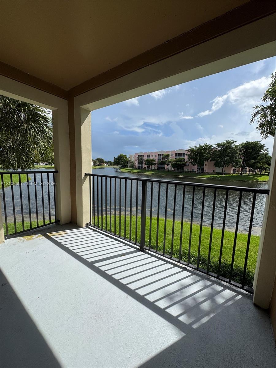 Covered balcony featuring concrete flooring and black metal railing, overlooking a water feature and landscaped grounds