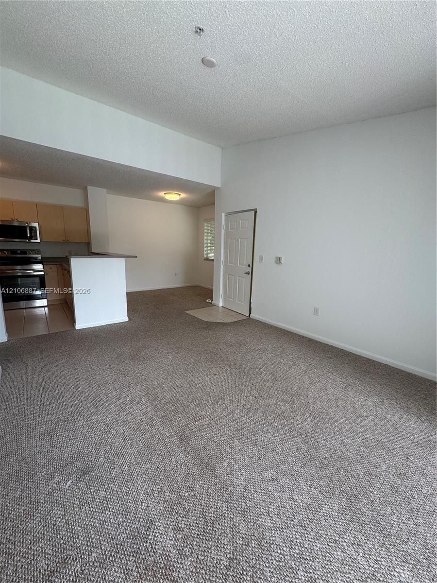 Open-concept interior featuring high vaulted ceilings, carpeted flooring, and a kitchen peninsula with integrated stainless steel appliances