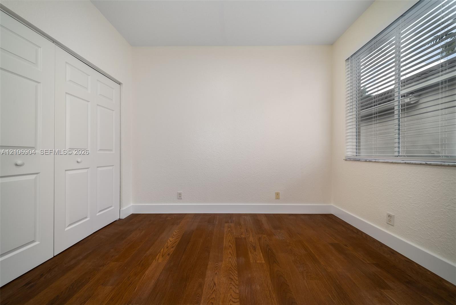Room featuring wood-finish flooring, white paneled closet doors, and a window with horizontal blinds