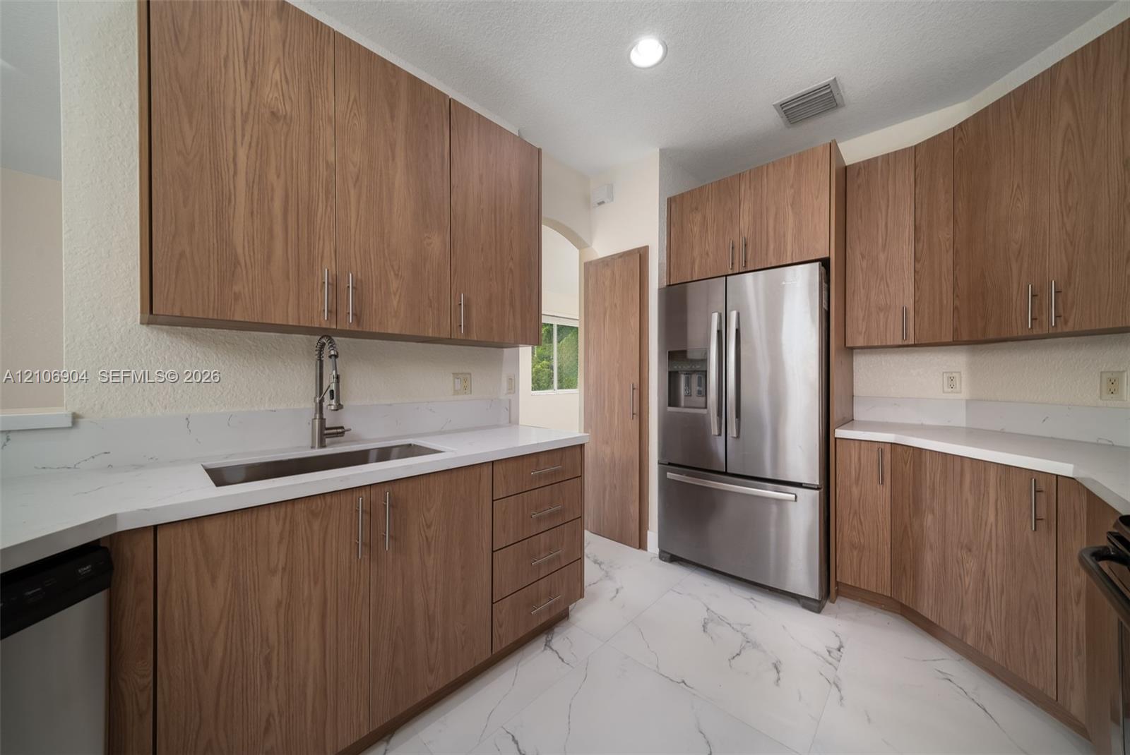 Kitchen featuring wood-finish cabinetry, quartz countertops, stainless steel appliances, and large-format tile flooring
