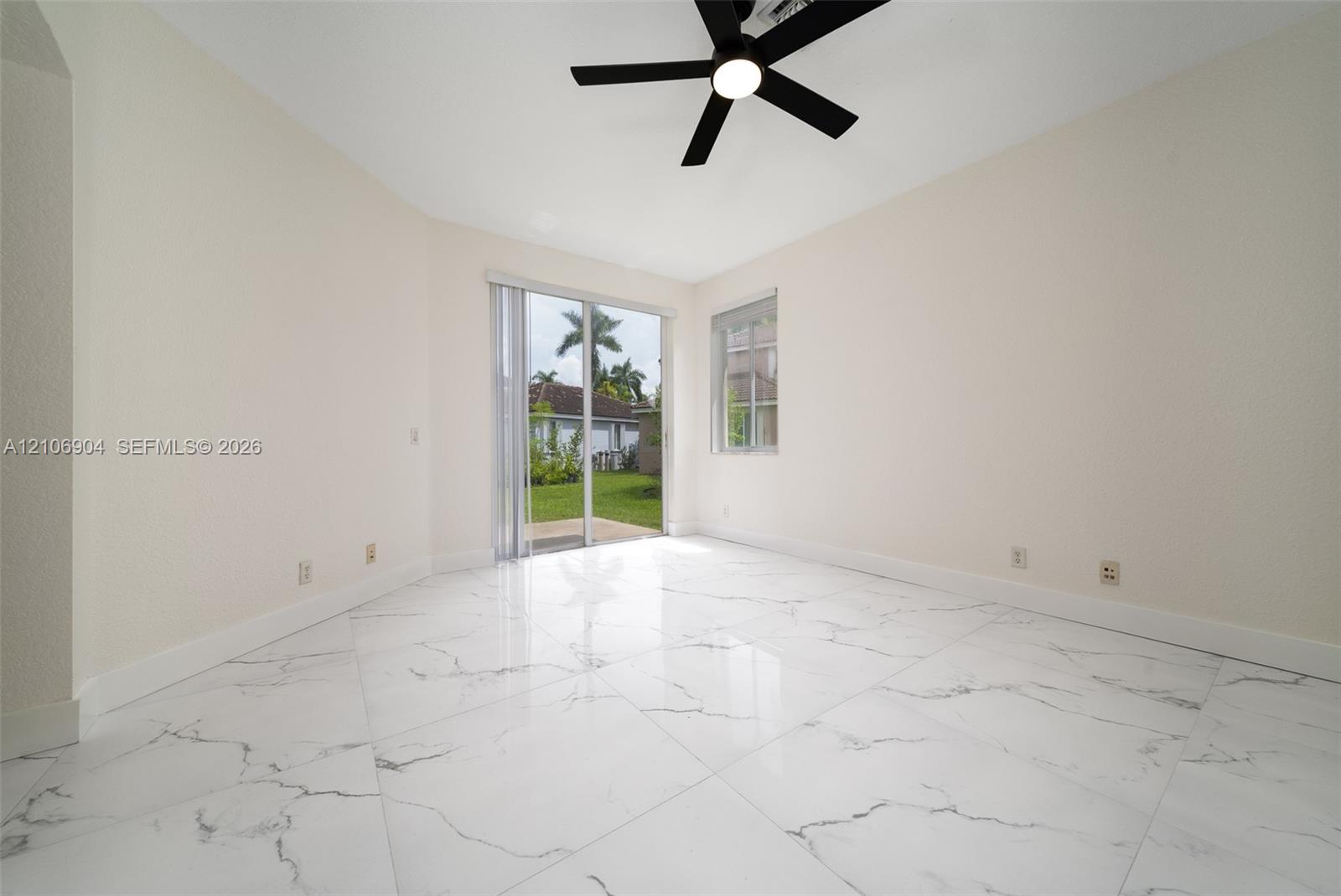 Interior space featuring large-format veined tile flooring, neutral wall tones, a black ceiling fan with integrated lighting, and a sliding glass door