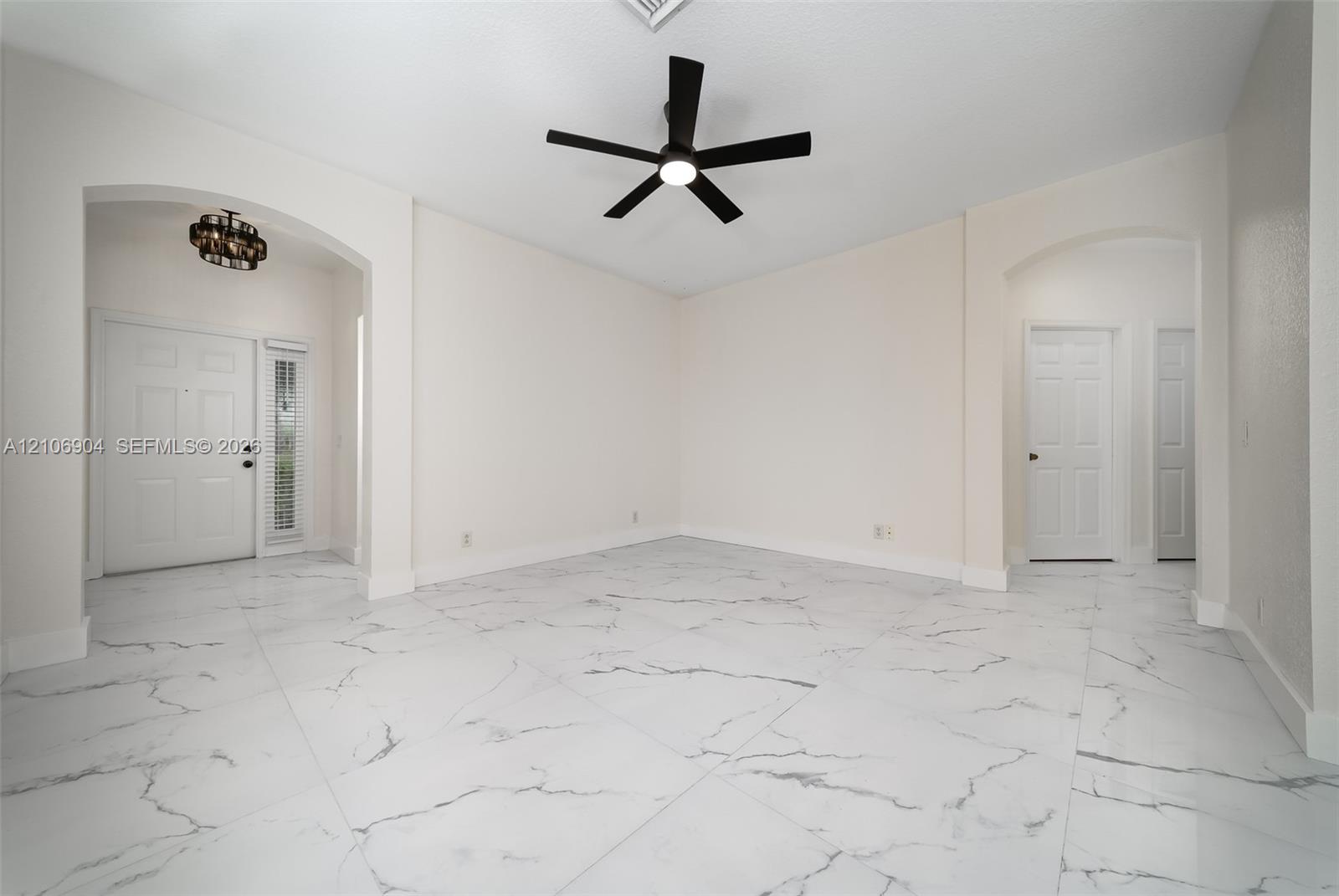Large-format tile flooring with a neutral-toned veined pattern, recessed archways, matte black ceiling fan with integrated lighting, and multi-panel entry door featuring a vertical glass sidelight