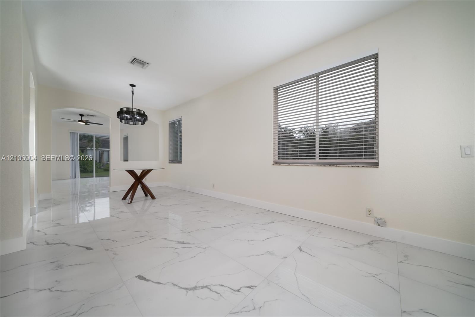 Large-format white tile flooring with grey veining, arched entryway, multi-light metal chandelier, and horizontal window blinds