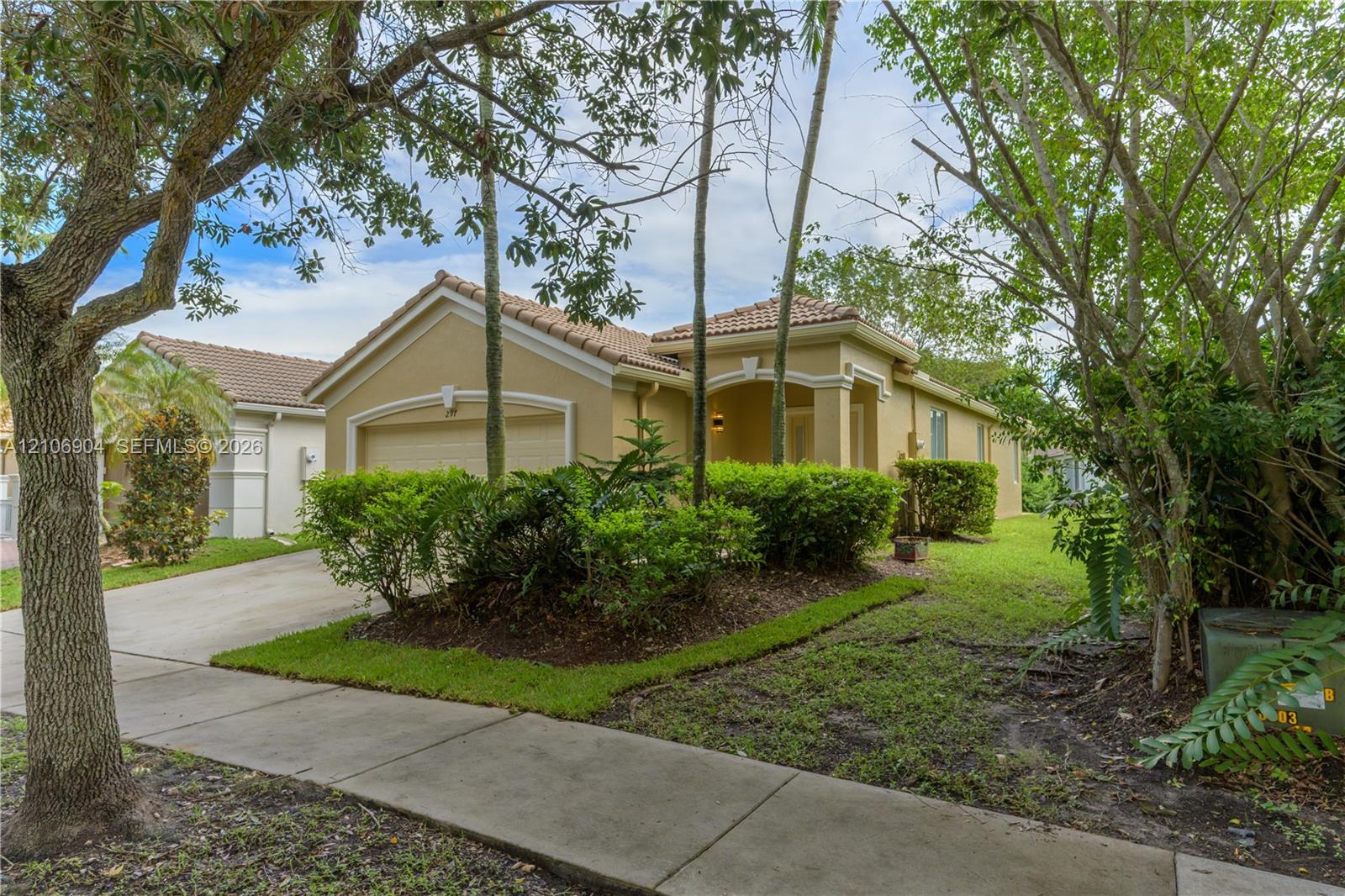 Stucco exterior with a tiled roof, arched entryway, and attached garage, complemented by mature landscaping and a concrete driveway