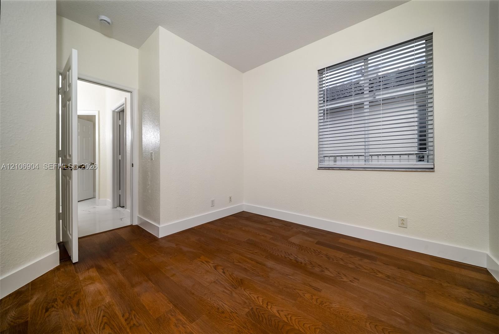 Room featuring wood-finish flooring, neutral wall paint, and a window with horizontal blinds