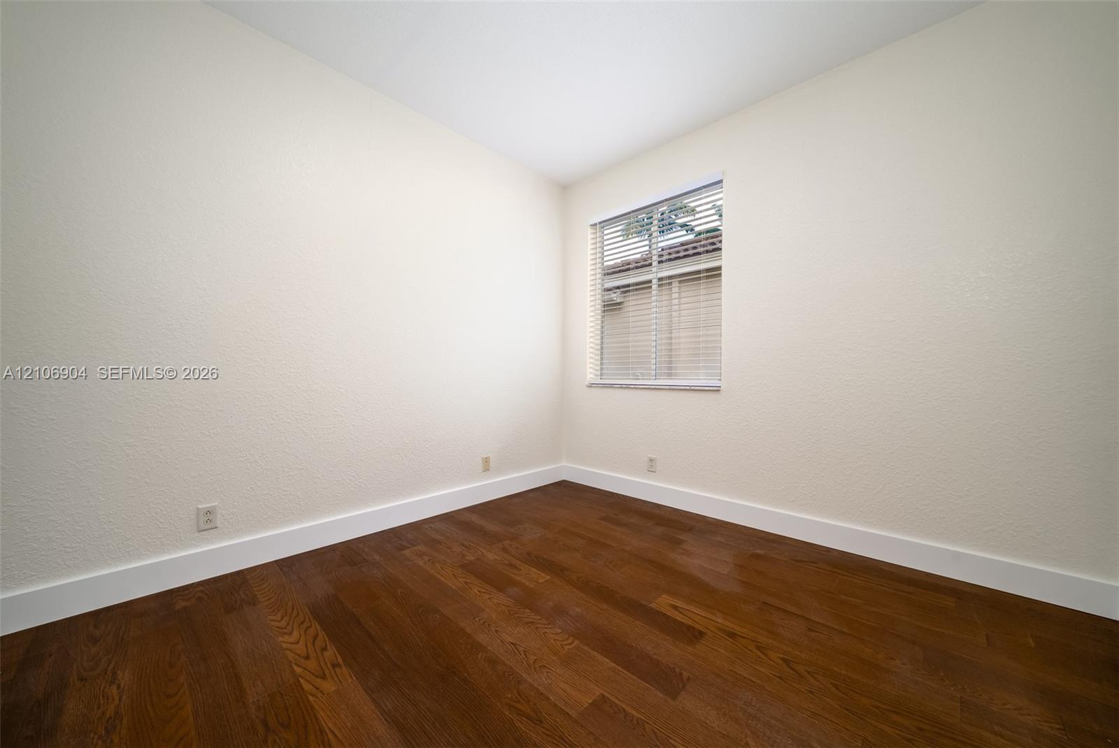 Interior room featuring wood-finish flooring, neutral wall tones, and a window with horizontal blinds
