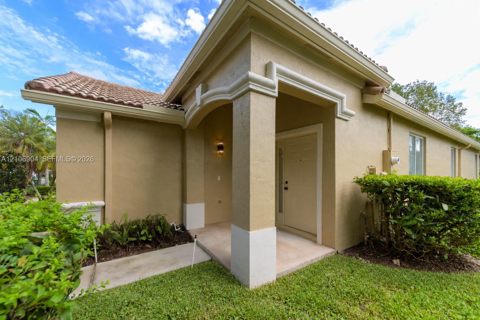 Stucco exterior featuring a covered entryway, arched architectural detailing, a tiled roof, and a concrete walkway