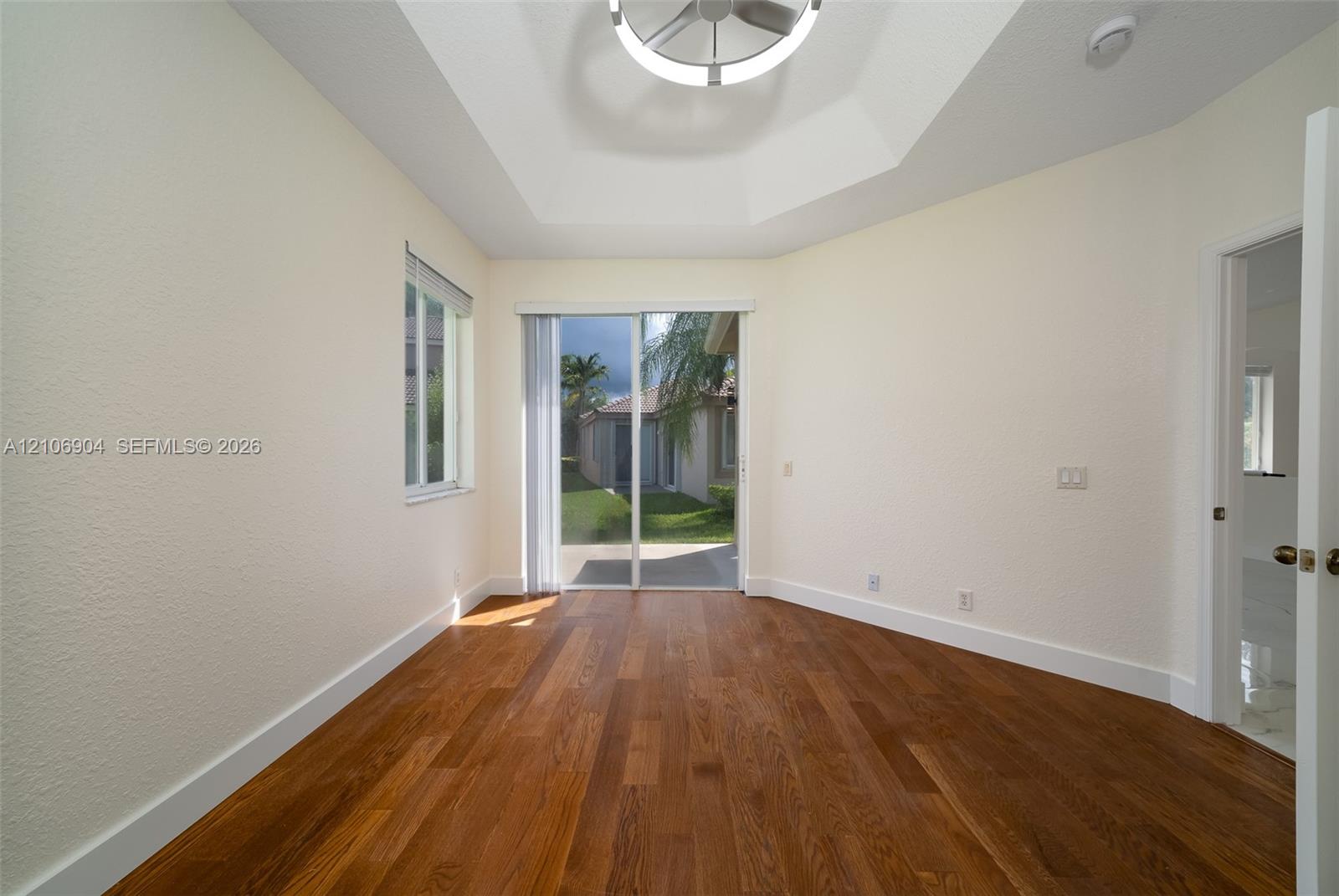 Room featuring wood-finish flooring, tray ceiling with circular LED fixture, and sliding glass door with exterior access