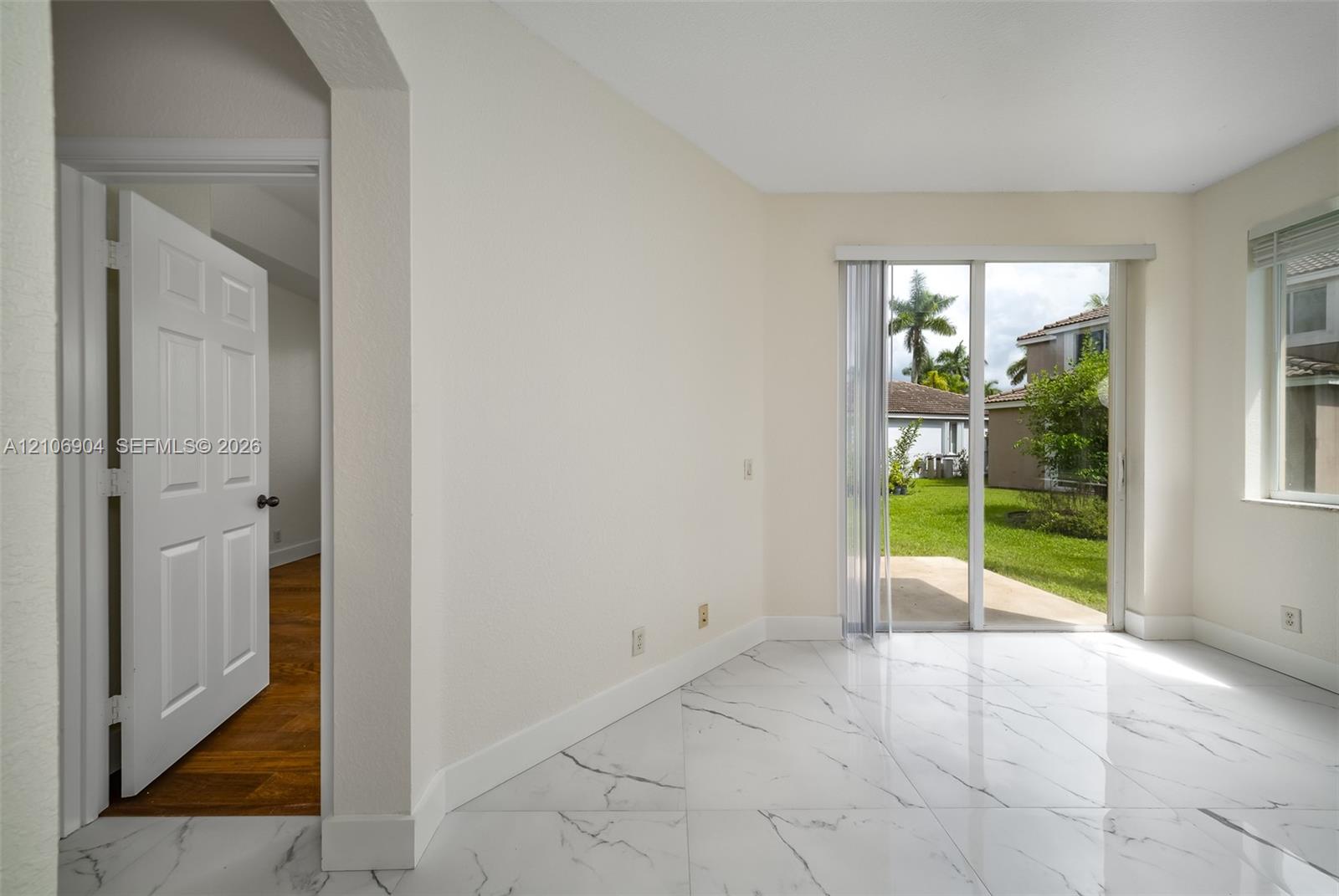 Interior featuring large-format white stone-finish flooring with dark veining, sliding glass patio doors, and a six-panel interior door