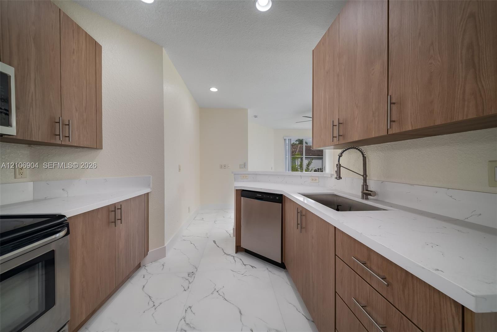 Kitchen featuring wood-finish cabinetry, white stone-patterned countertops, stainless steel appliances, and tile flooring with a marble pattern