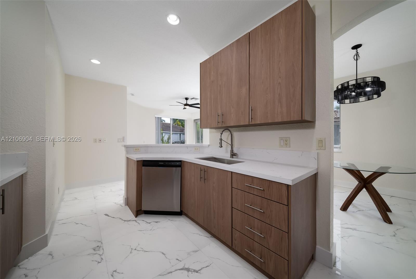 Kitchen featuring wood-finish cabinetry, white stone-patterned countertops, recessed lighting, and large-format porcelain tile flooring