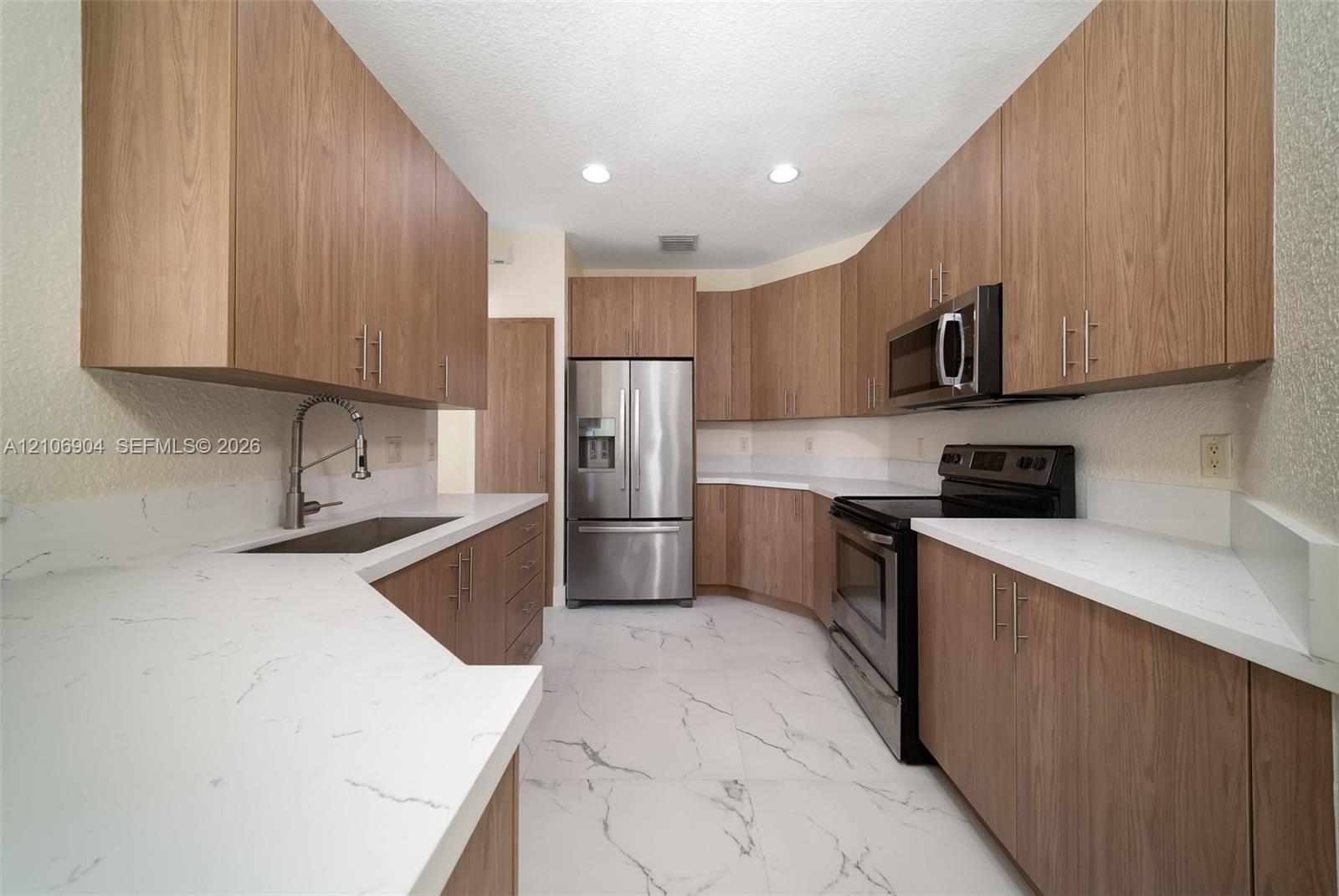 Kitchen featuring wood-finish cabinetry, quartz countertops, stainless steel appliances, and large-format tile flooring