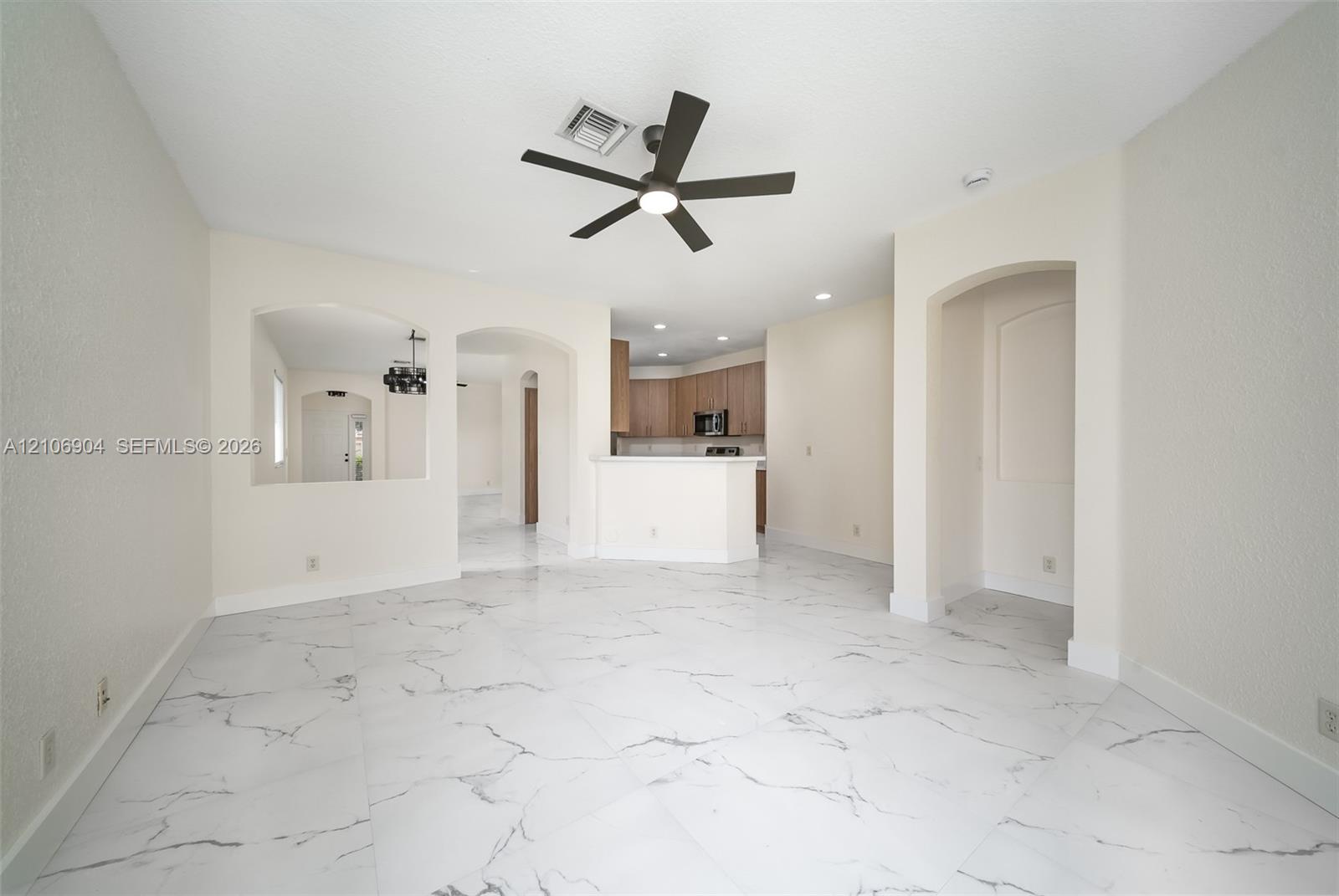 Large-format white tile flooring with veining detail, multi-blade ceiling fan with integrated lighting, arched wall openings, and recessed ceiling lighting