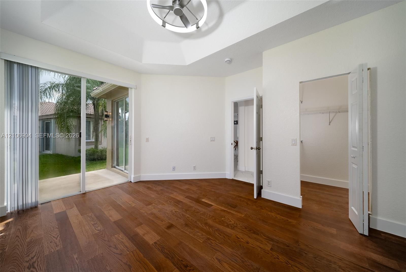 Tray ceiling with integrated fan and lighting, wood-finish flooring, sliding glass door, and walk-in closet with wire shelving