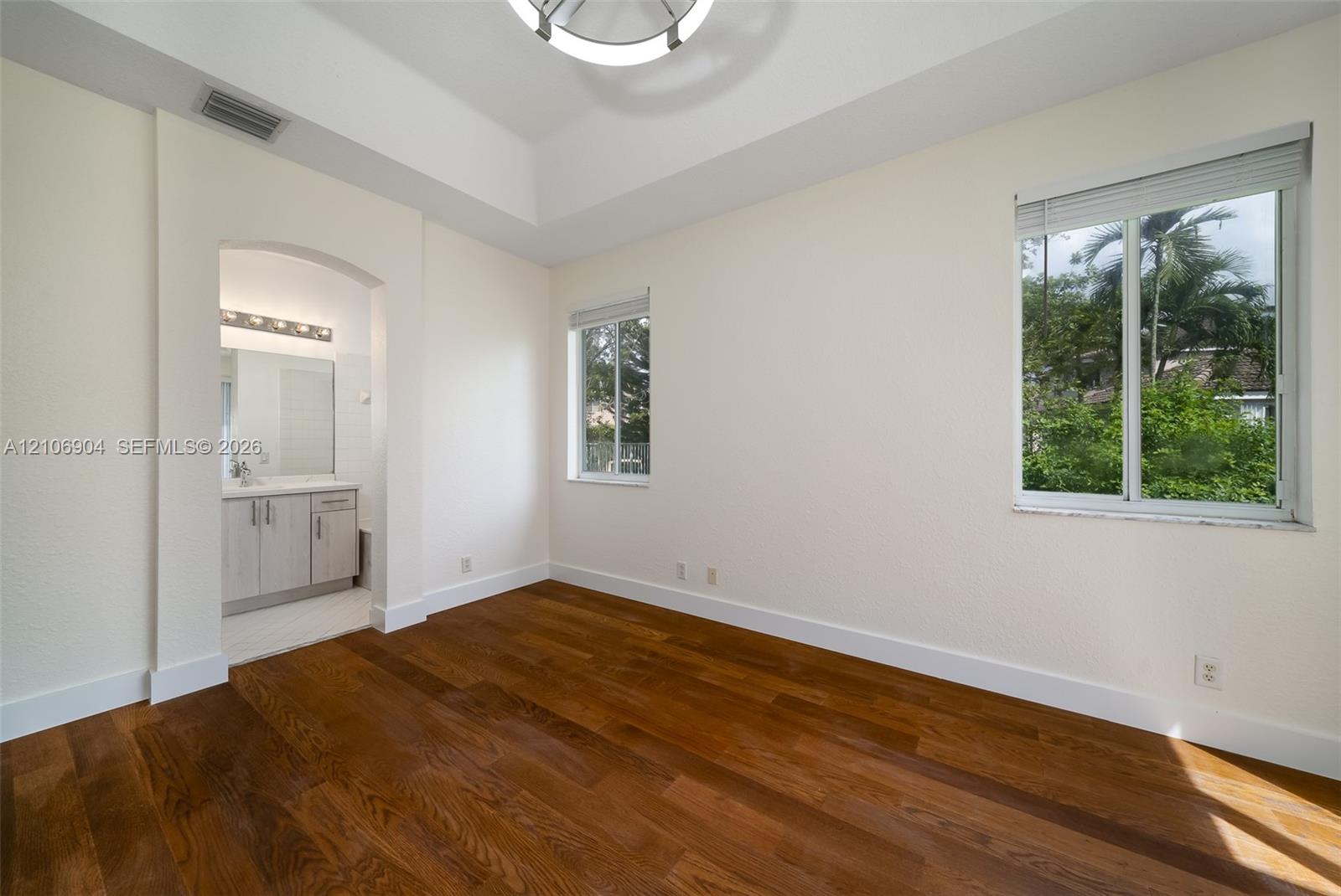 Room featuring wood-finish flooring, tray ceiling, arched entryway, and multiple windows with horizontal blinds