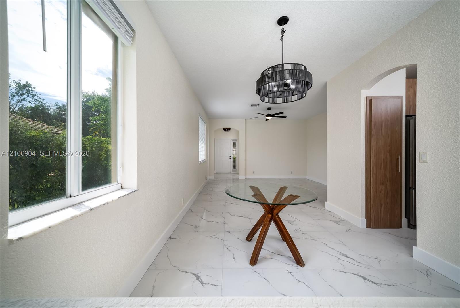 Large-format stone-finish tile flooring, decorative multi-tiered drum chandelier, recessed ceiling lighting, arched entryway, and dual-pane windows