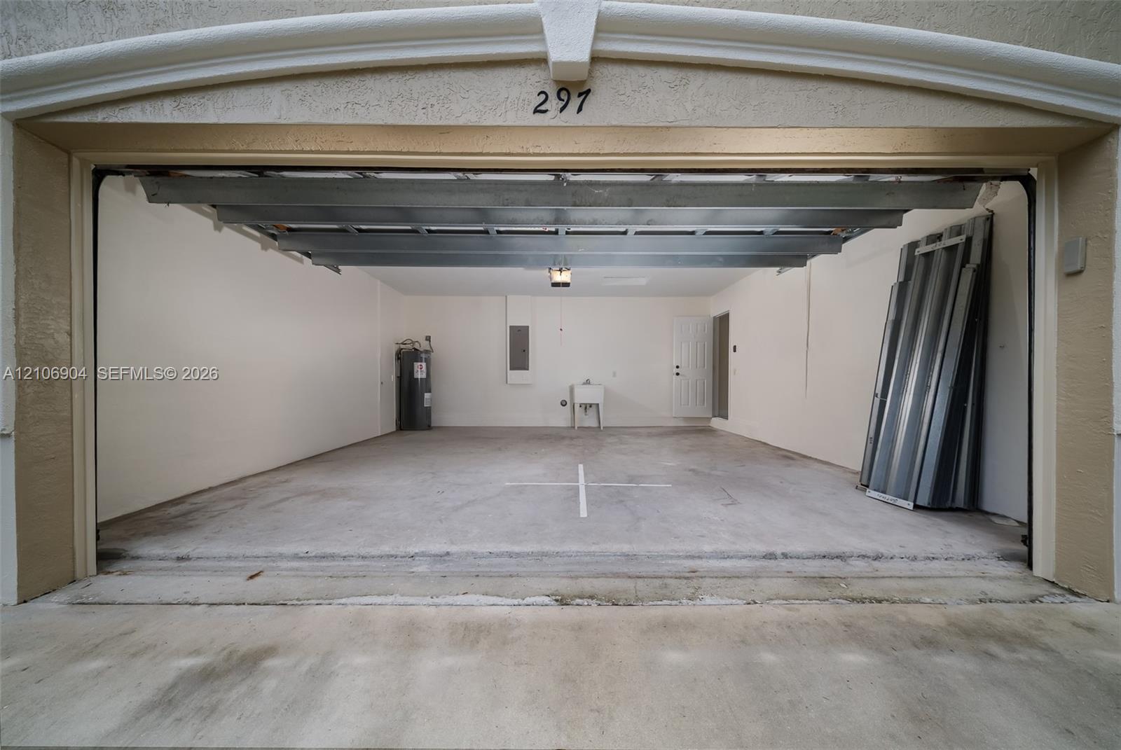 Enclosed garage featuring a concrete floor, integrated utility sink, overhead lighting, and dedicated water heater enclosure