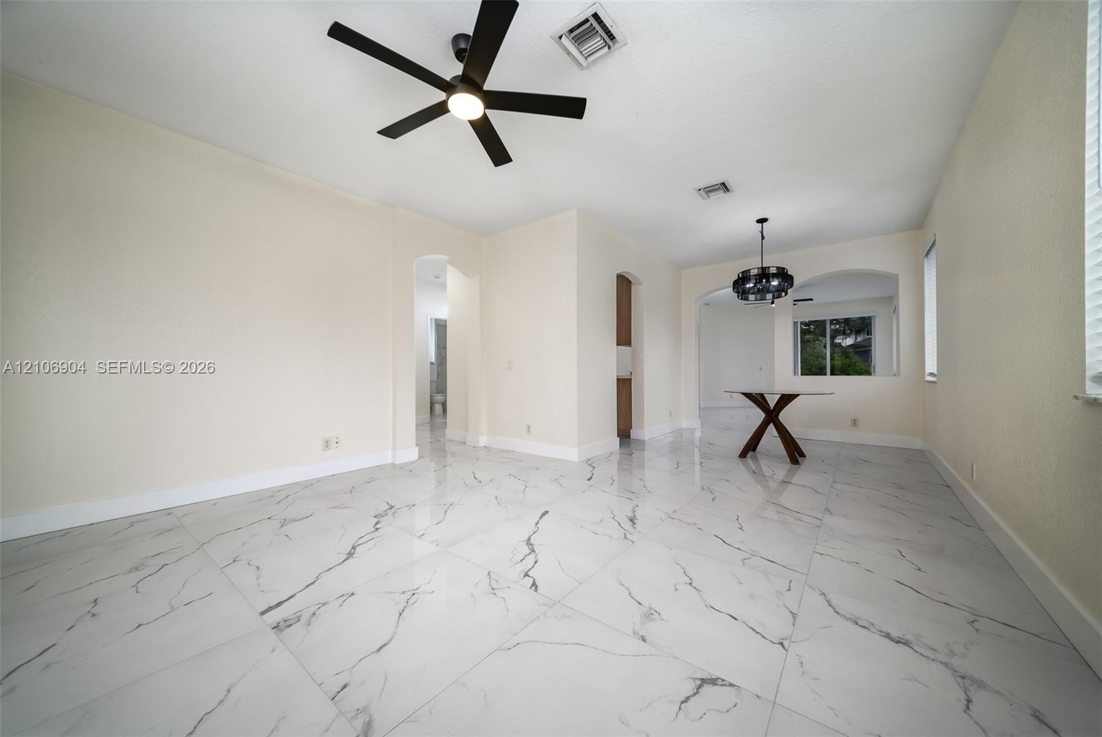 Large-format tile flooring with marble-pattern veining, matte black ceiling fan, and decorative chandelier featuring geometric hardware