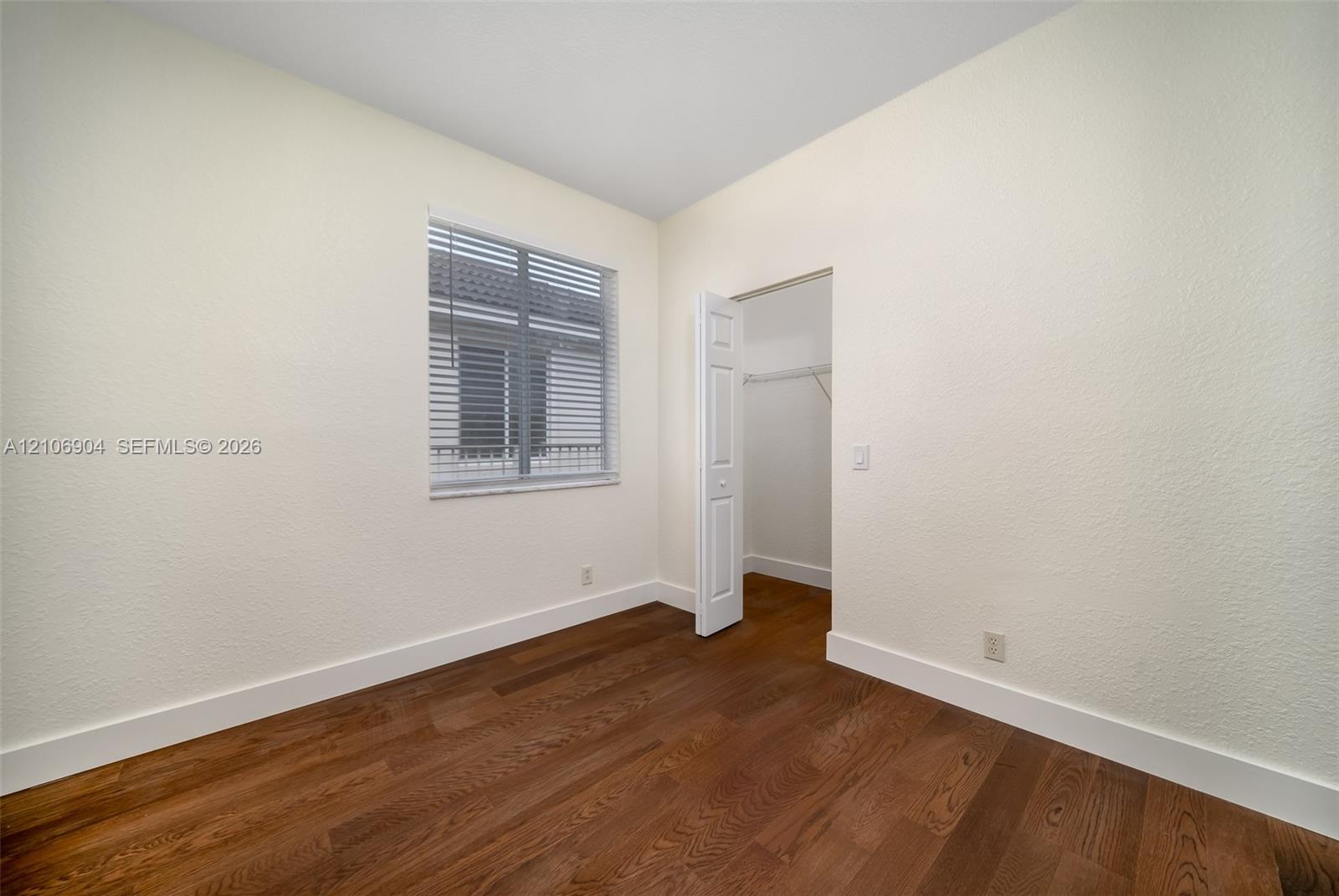 Wood-finish flooring, neutral wall tones, window with horizontal blinds, and a closet with a bifold door