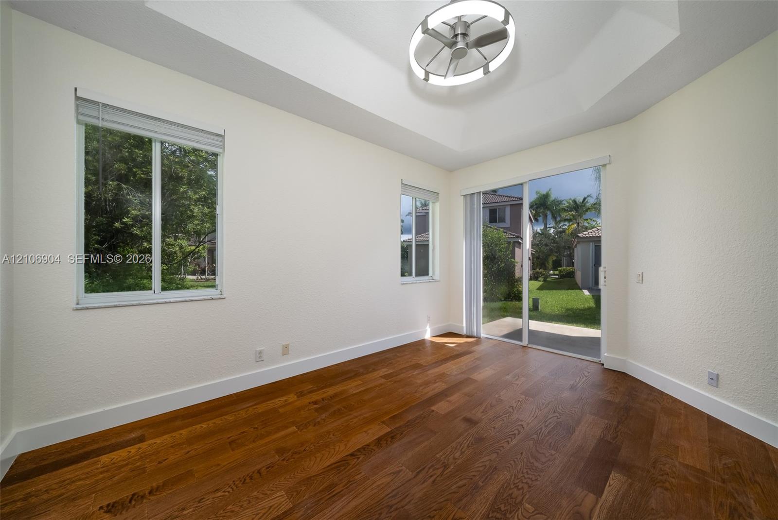 Tray ceiling with integrated circular lighting, wood-finish flooring, and sliding glass door access to the exterior