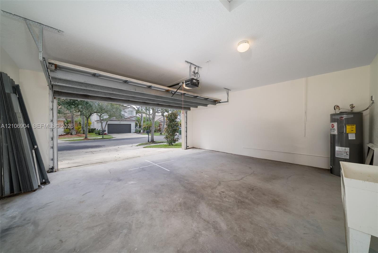 Multi-car garage featuring a concrete floor, automated overhead door, ceiling-mounted opener, water heater, and utility basin