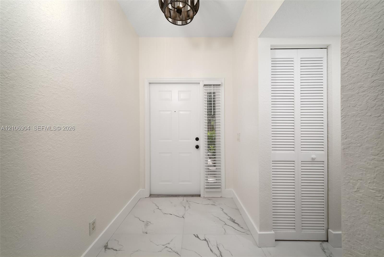 Entryway featuring large-format veined tile flooring, a multi-panel door with a sidelight, a louvered-panel closet door, and a circular drum pendant light fixture