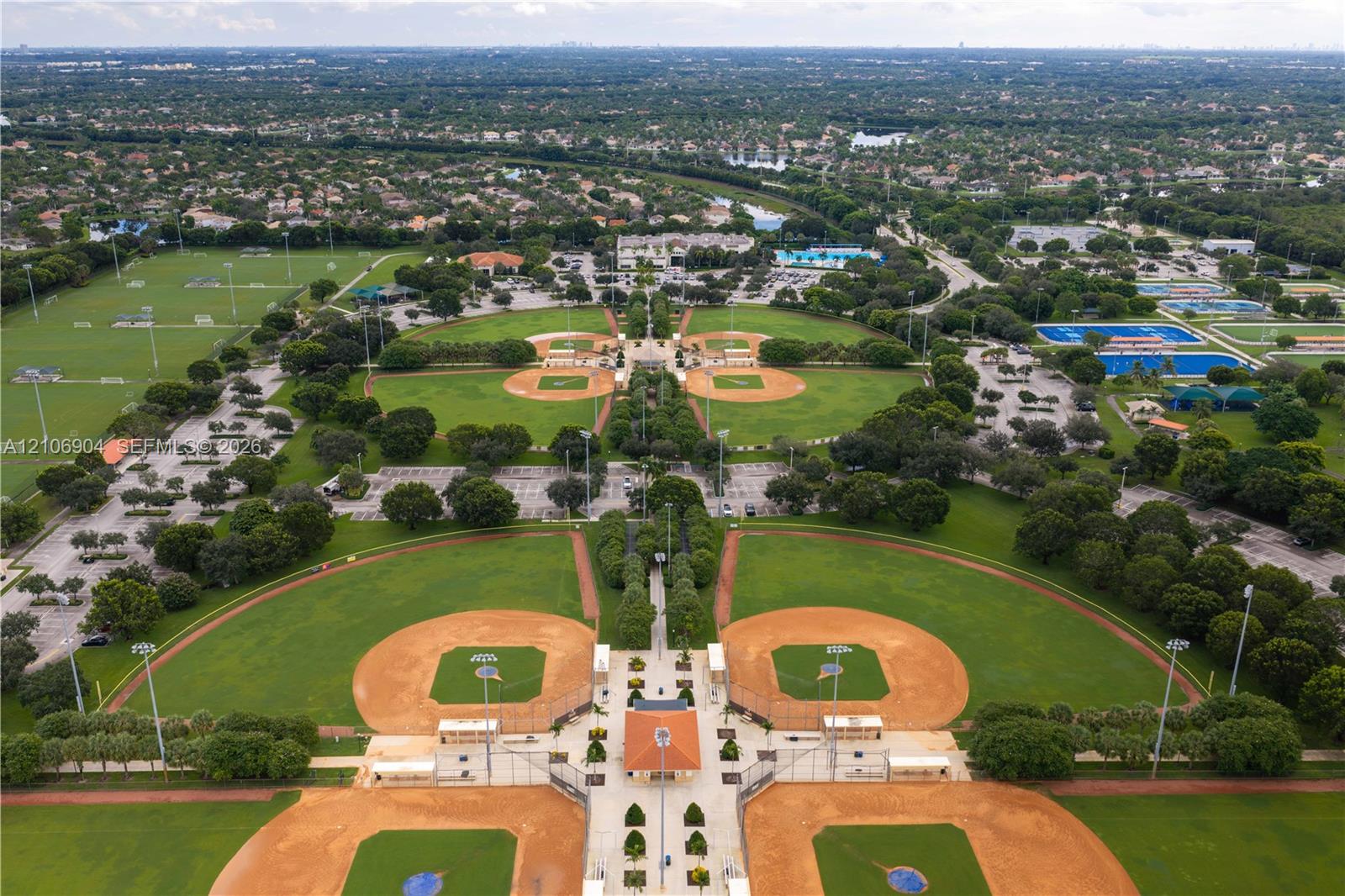 Aerial perspective of a large-scale recreational complex featuring multiple baseball diamonds, manicured grass fields, paved parking areas, and mature landscaping