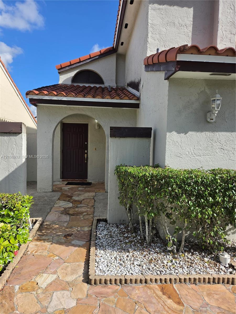 Stucco exterior featuring a covered entryway with a terracotta-style tiled roof, arched architectural details, and natural stone paver walkway