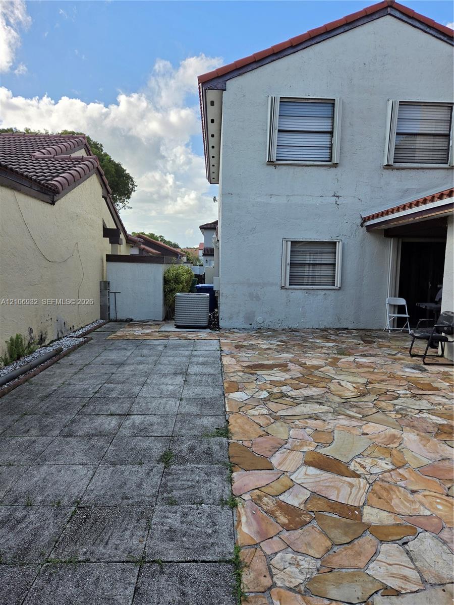 Exterior patio area featuring a combination of rectangular concrete pavers and natural stone flagstone surfacing, paired with a stucco-finish building facade, tiled roofline, and window shutters