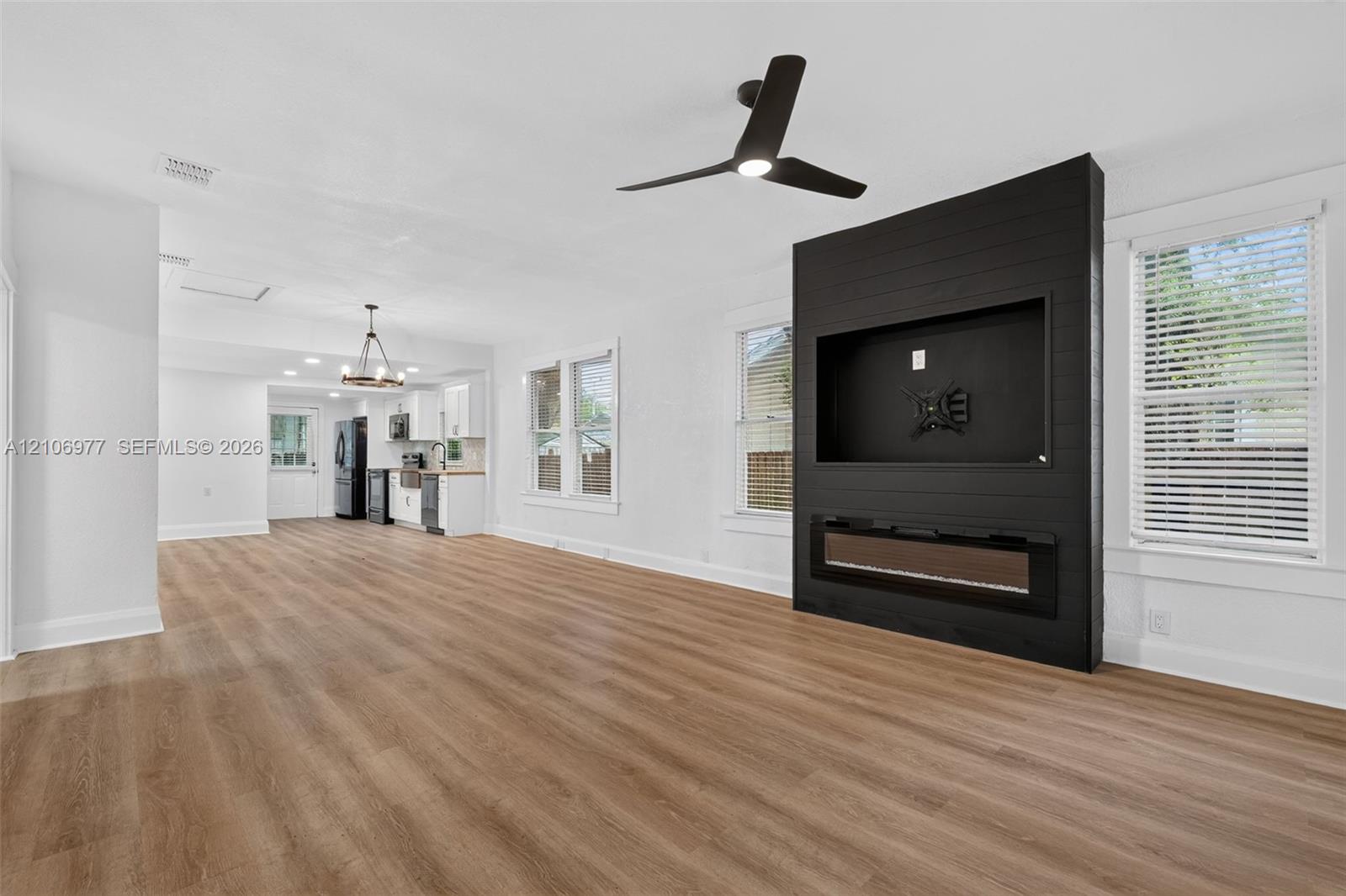 Open-concept space featuring wood-finish flooring, a matte black shiplap accent wall with a built-in electric fireplace, and a three-blade ceiling fan