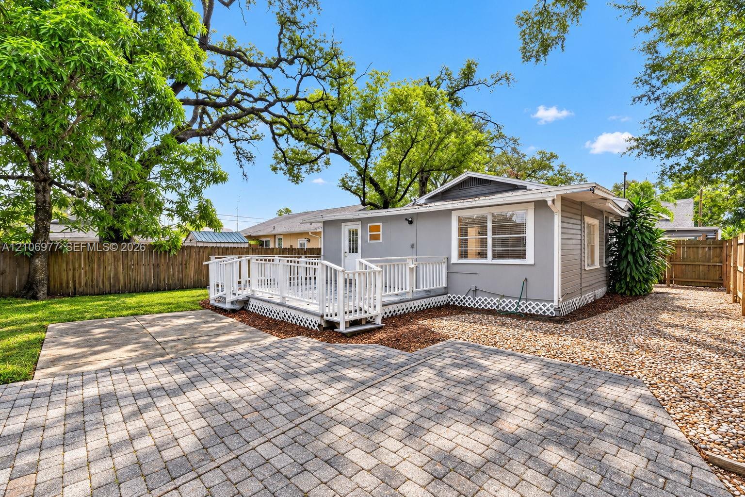 Exterior rear elevation featuring a raised white wooden deck, paver stone patio, gravel surfacing, and wood privacy fencing