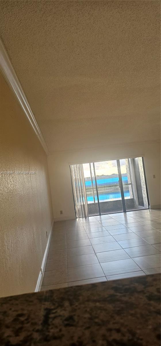 Interior space featuring neutral-toned tile flooring, textured ceiling, crown molding, and sliding glass doors leading to a balcony