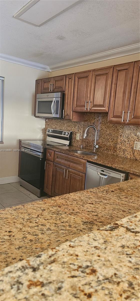 Kitchen featuring raised-panel wood cabinetry, natural stone countertops, stainless steel appliances, and an undermount sink with a gooseneck faucet Kitchen featuring raised-panel wood cabinetry, natural stone countertops, stainless steel appliances, and an undermount sink with a gooseneck faucet