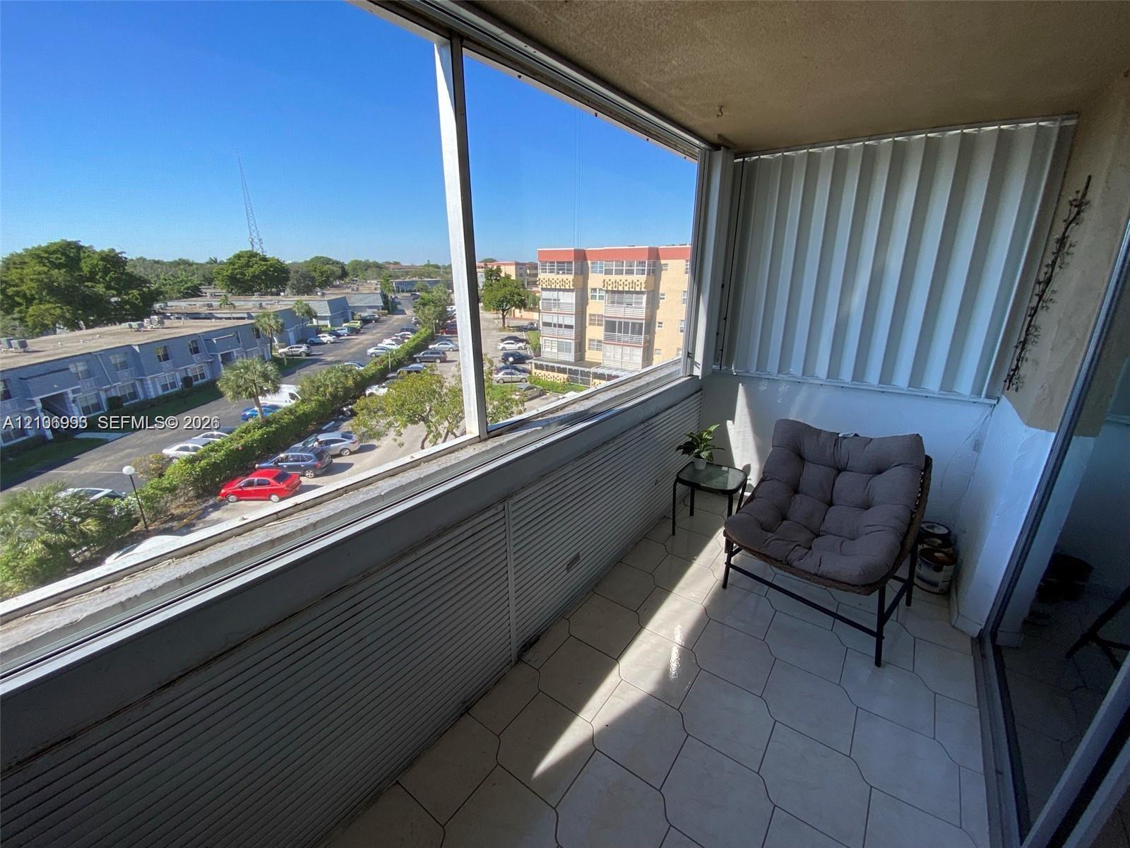 Enclosed balcony featuring tile flooring, floor-to-ceiling glass paneling, and accordion-style storm shutters
