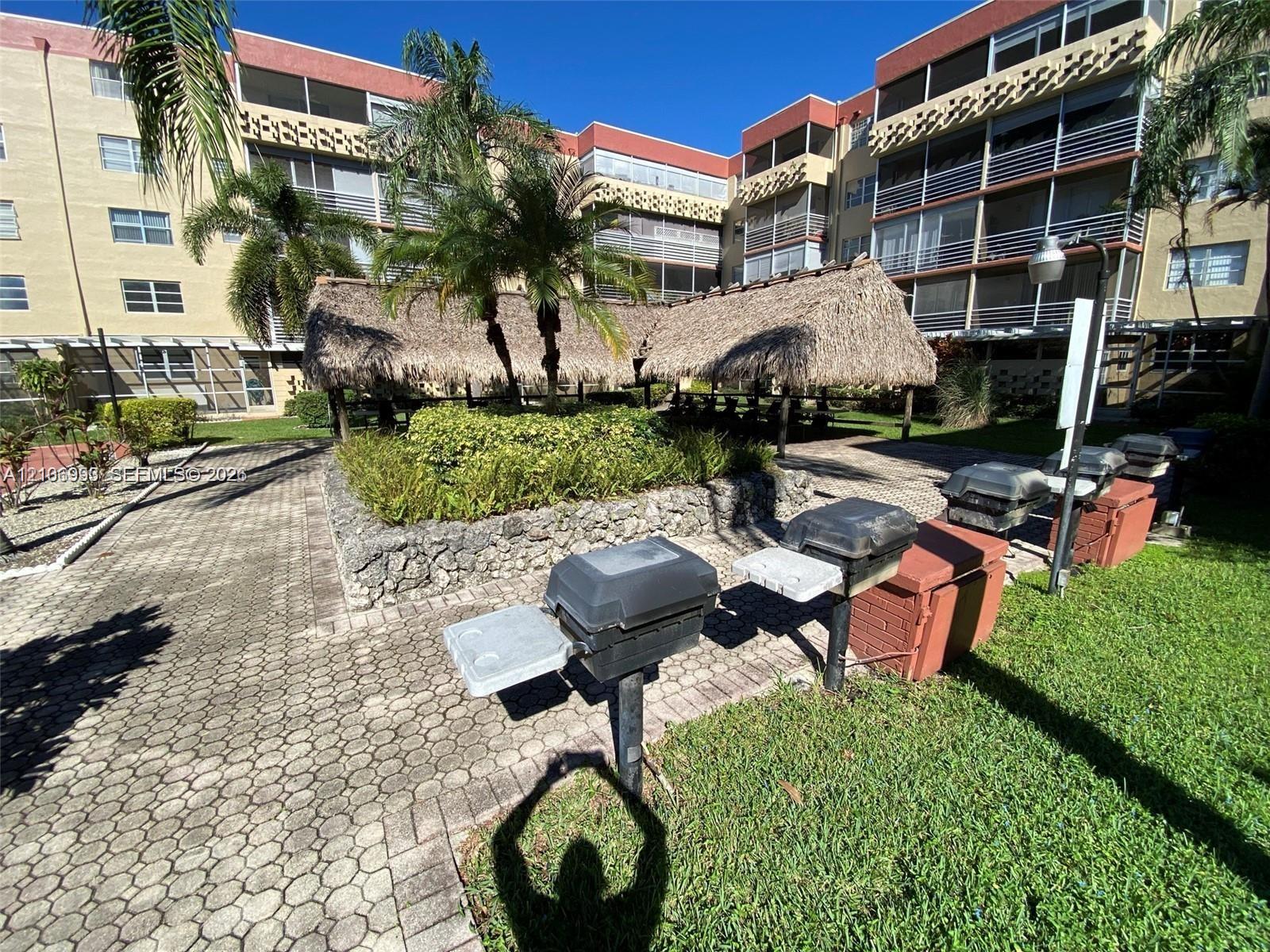 Common area featuring a paved brick patio, thatched-roof tiki hut, stone-lined landscaping, built-in charcoal grills, and mature palm trees
