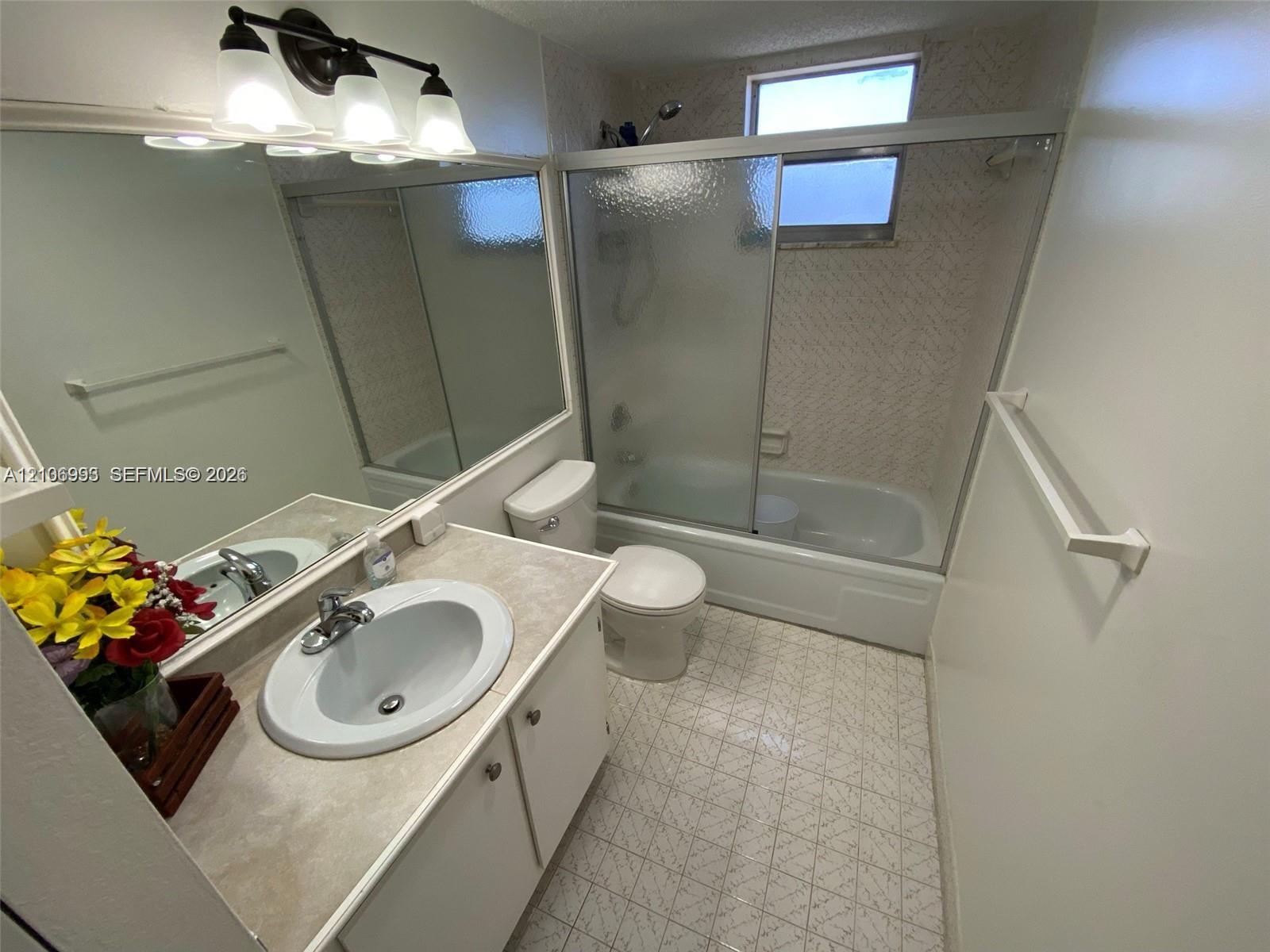 Bathroom featuring a vanity with a drop-in sink, a large wall-mounted mirror, a tub-shower combination with sliding glass doors, and tiled flooring