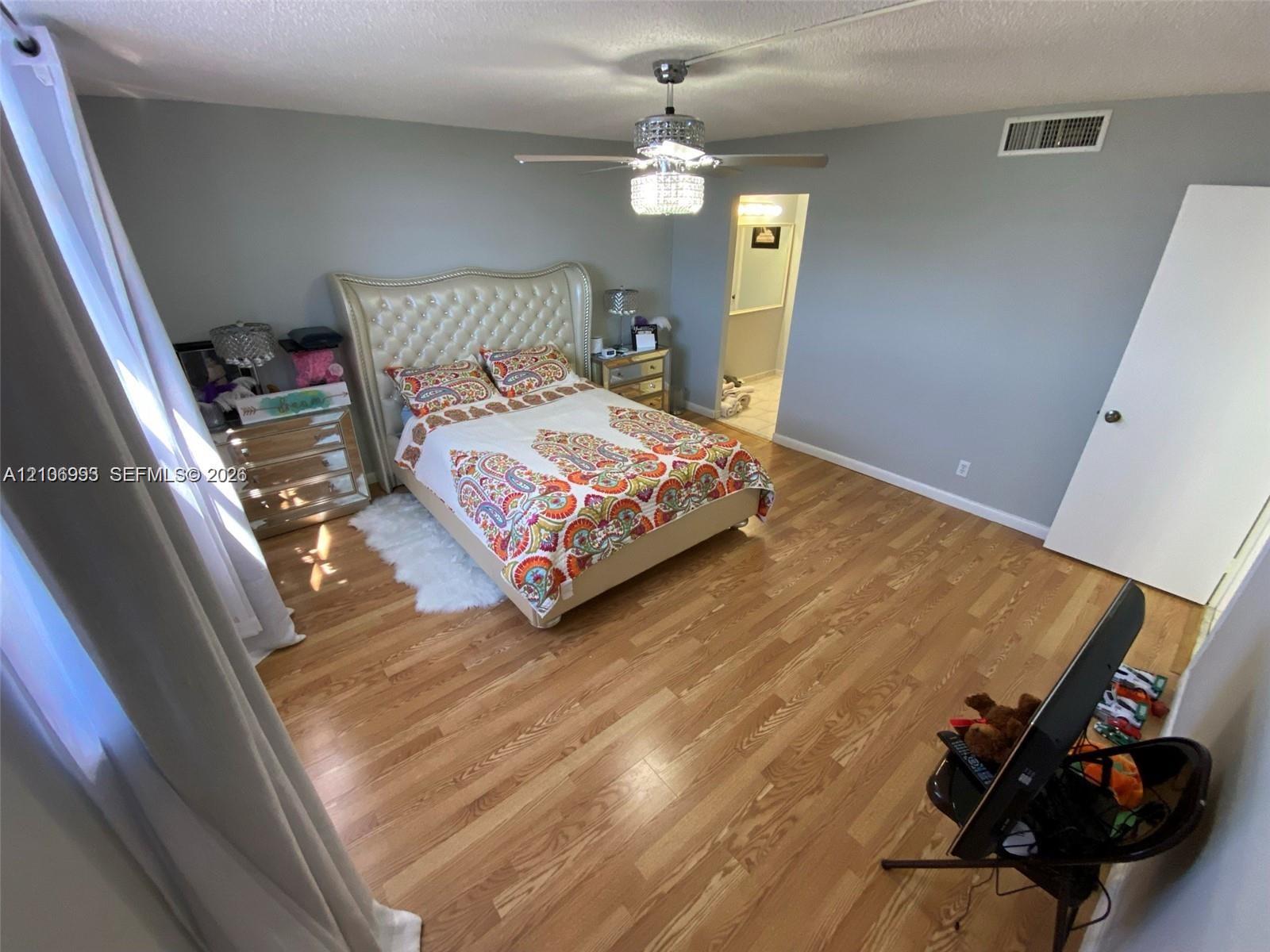 Bedroom featuring wood-finish flooring, a multi-blade ceiling fan with an integrated crystal-style light fixture, and neutral wall paint