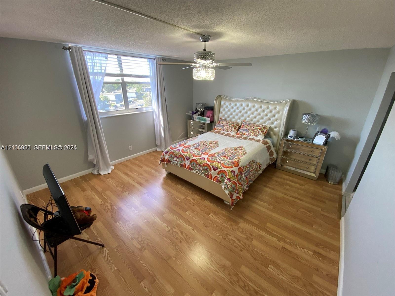 Bedroom featuring wood-finish flooring, a crystal-accented ceiling fan with integrated lighting, and a window with horizontal blinds
