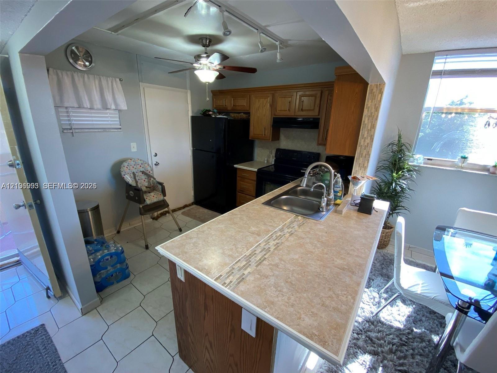 Kitchen featuring wood cabinetry, a breakfast bar with stone-finish countertop, dual-basin stainless steel sink with pull-down faucet, and ceramic tile flooring