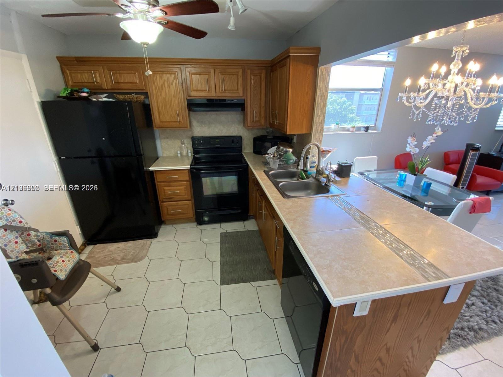 Kitchen featuring wood cabinetry, a tiled countertop peninsula with an integrated double basin sink, and hexagonal floor tile