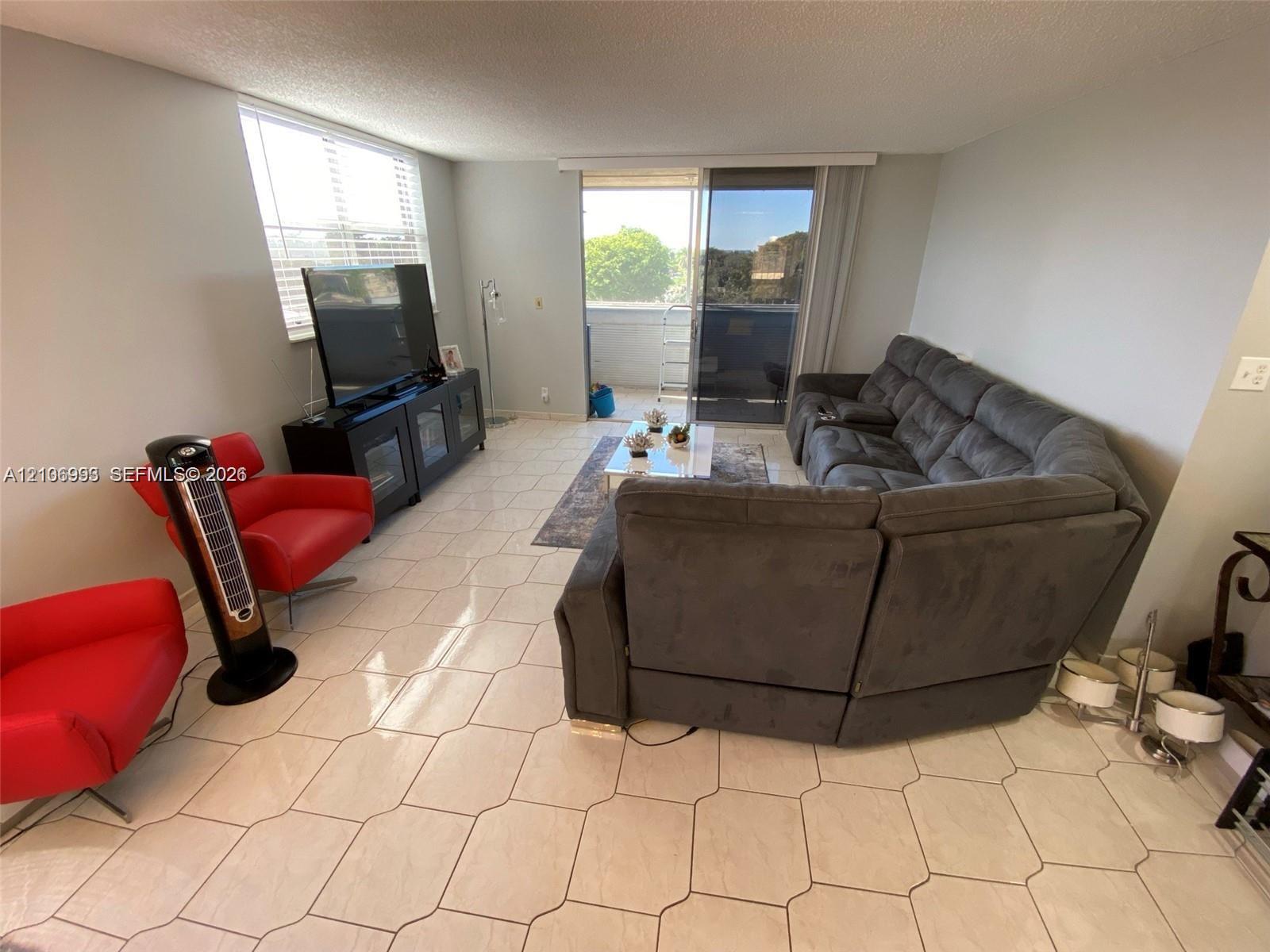 Neutral-toned living space featuring light-colored tile flooring, window blinds, and sliding glass doors with access to an exterior balcony