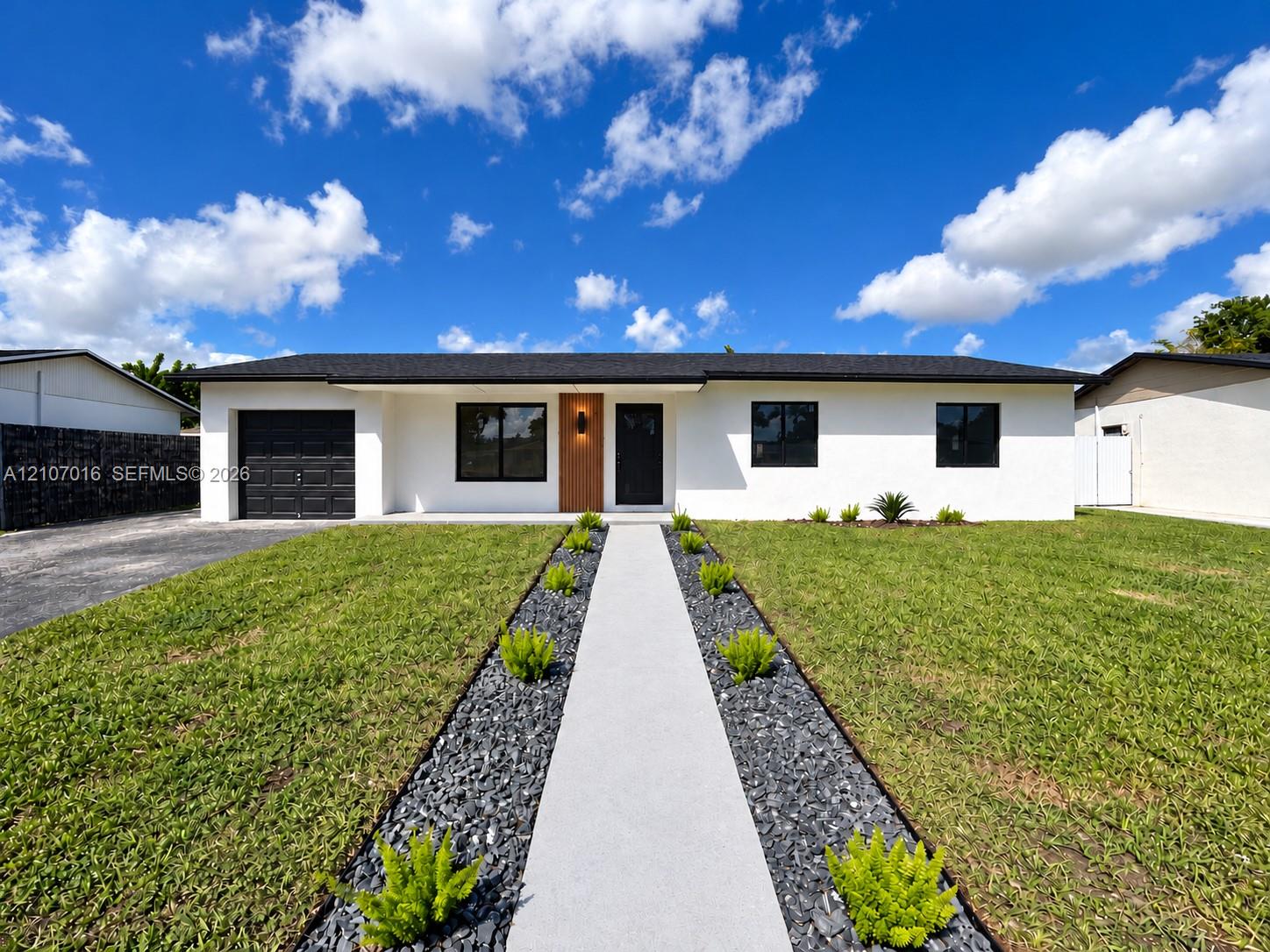 Single-story exterior featuring a stucco facade, dark-toned garage door, contemporary front door with wood-grain finish, asphalt shingle roof, and a paved walkway bordered by decorative stone and greenery Single-story exterior featuring a stucco facade, dark-toned garage door, contemporary front door with wood-grain finish, asphalt shingle roof, and a paved walkway bordered by decorative stone and greenery