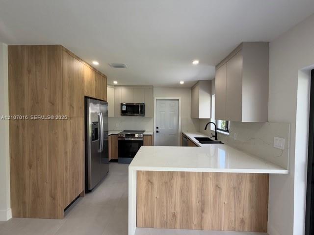 Kitchen featuring two-tone cabinetry with wood-finish accents, quartz countertops, integrated stainless steel appliances, and a matte black faucet