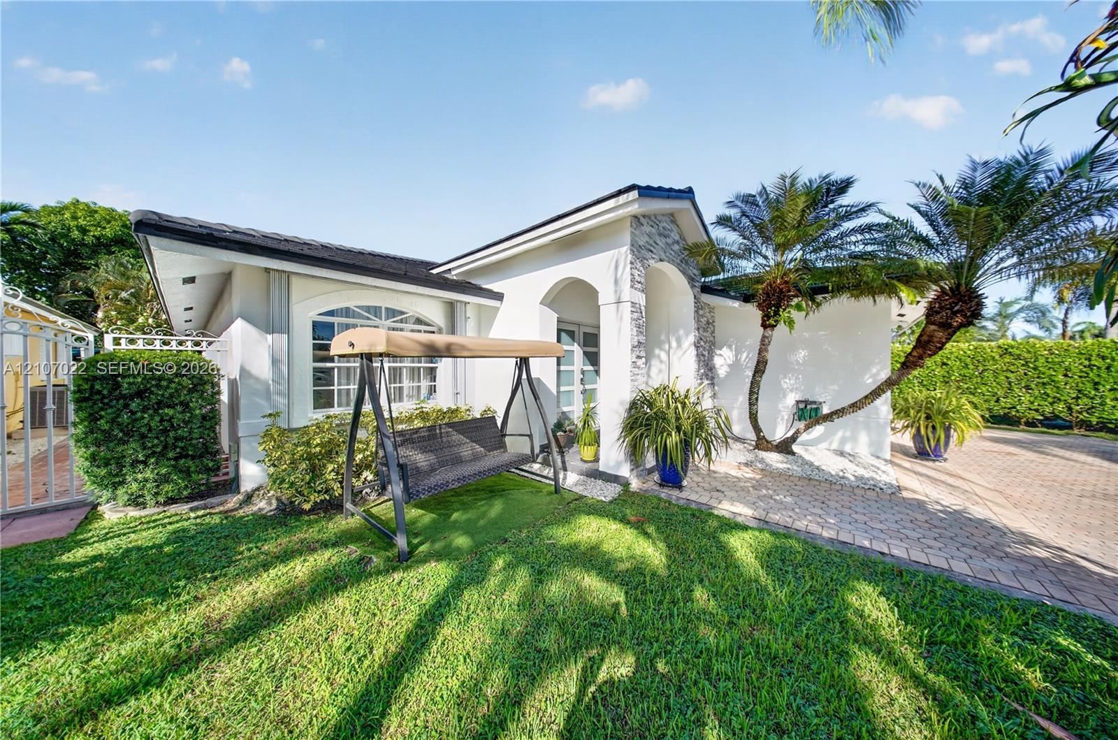 Exterior facade featuring a covered entryway with stone veneer detailing, arched architectural accents, decorative window mullions, and a paver driveway