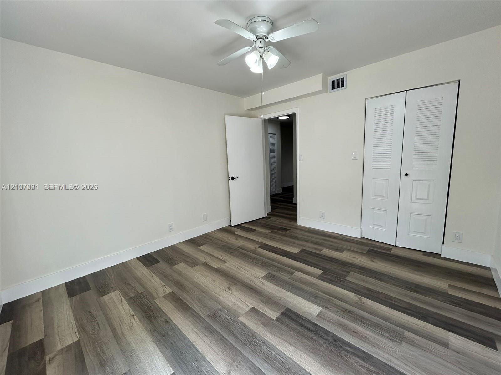Room featuring wood-finish flooring, a ceiling fan with integrated lighting, and a closet with bifold louvered doors