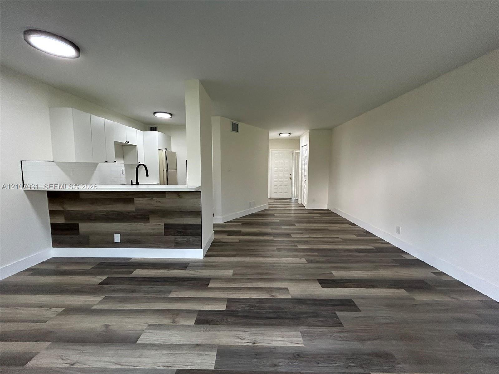 Wood-finish flooring throughout, white cabinetry, integrated kitchen peninsula with wood-accented face, matte black faucet, and flush-mount ceiling lighting