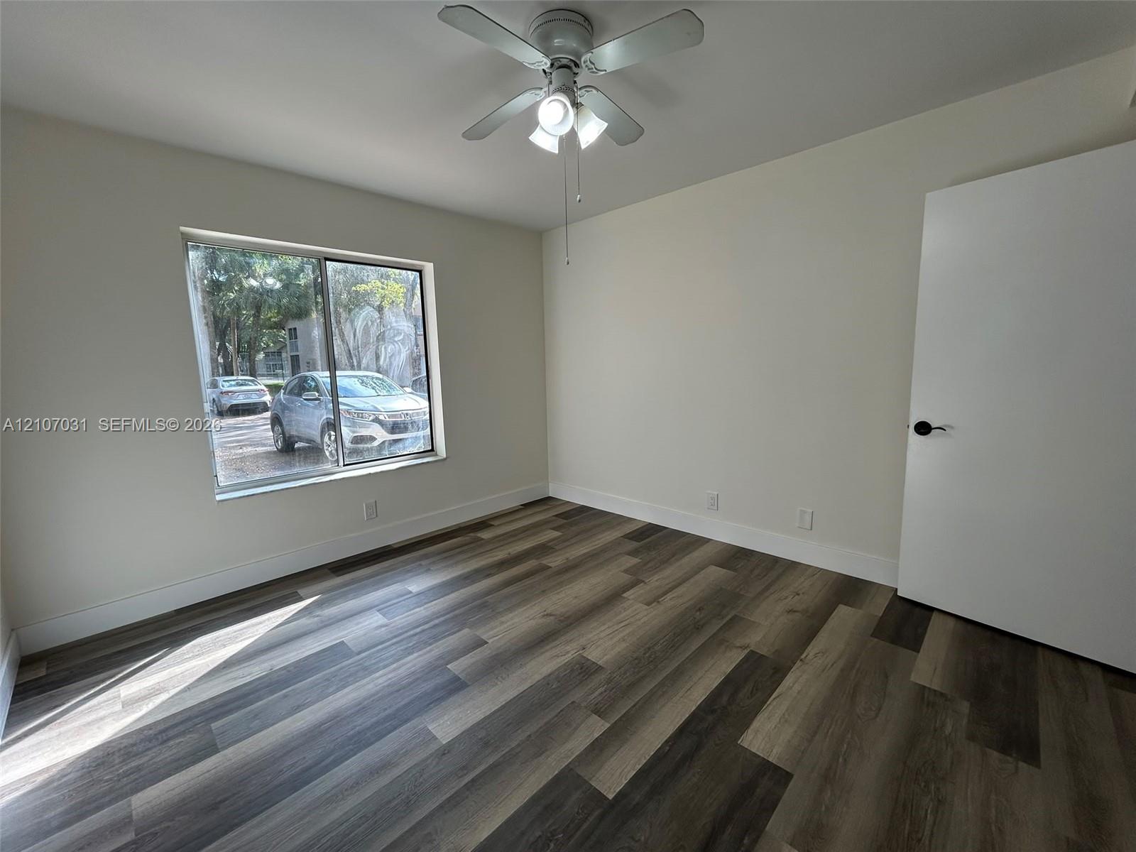 Room featuring wood-finish flooring, a neutral color palette, a sliding window, and a ceiling-mounted light fixture with a fan