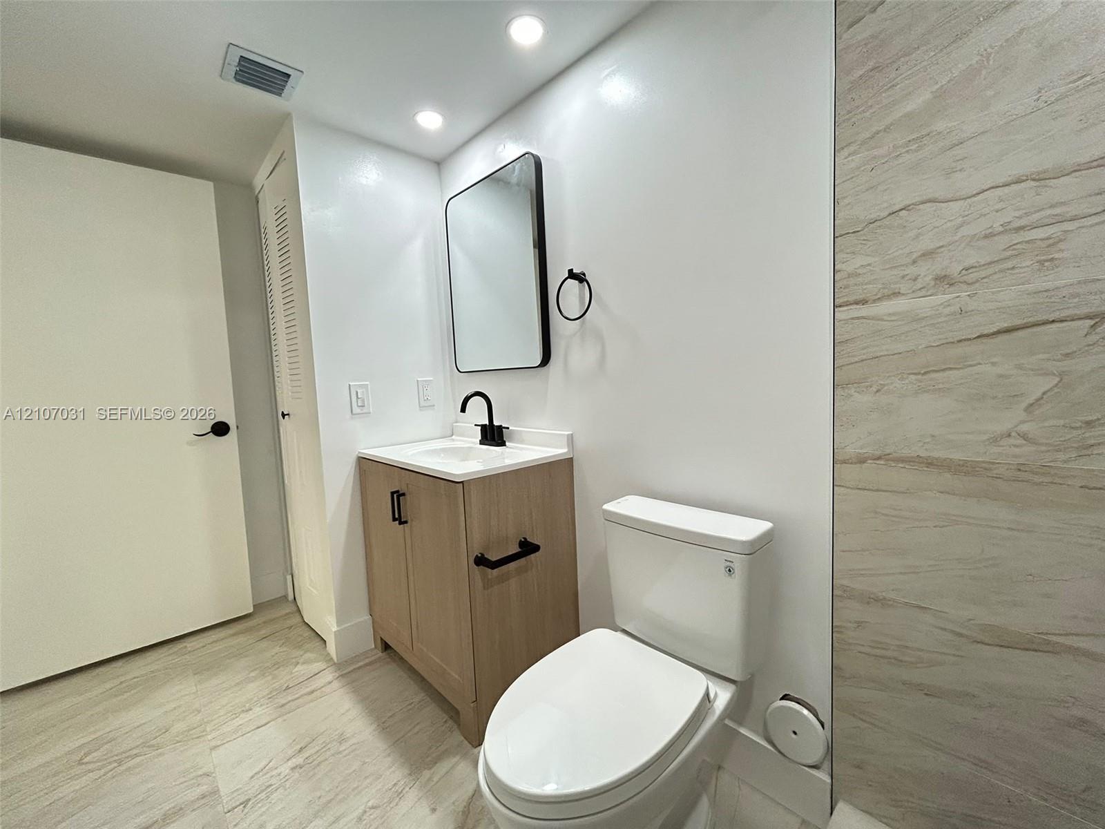 Modern vanity with wood-finish cabinetry, rectangular sink, and matte black hardware, paired with a rectangular mirror, recessed lighting, and tile wall surround